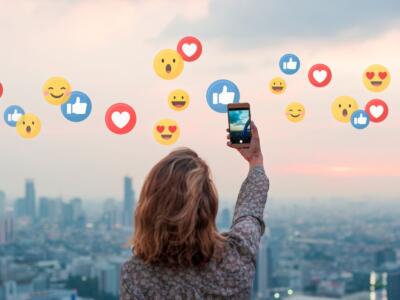 Ragazza con smartphone da cui escono reaction ed emoticon