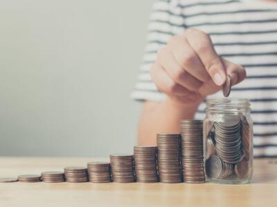 Hand,Of,Male,Putting,Coin,In,Jar,With,Money,Stack