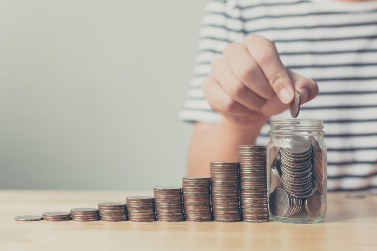 Hand,Of,Male,Putting,Coin,In,Jar,With,Money,Stack