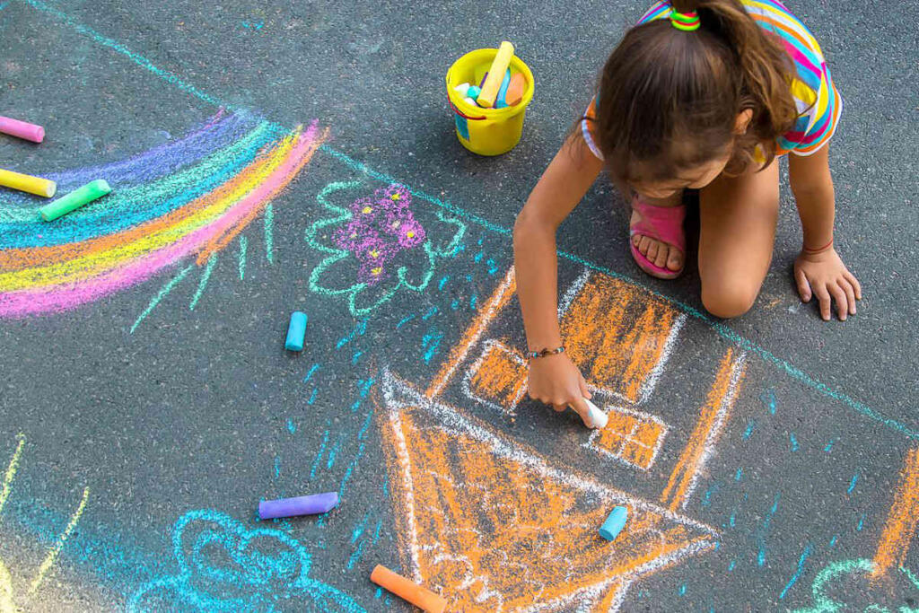 Bambina che disegna sull'asfalto con gessetti colorati