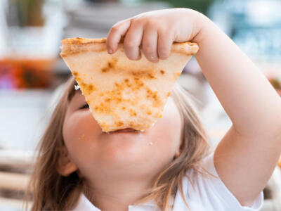 Una bambina mangia una fetta di pizza