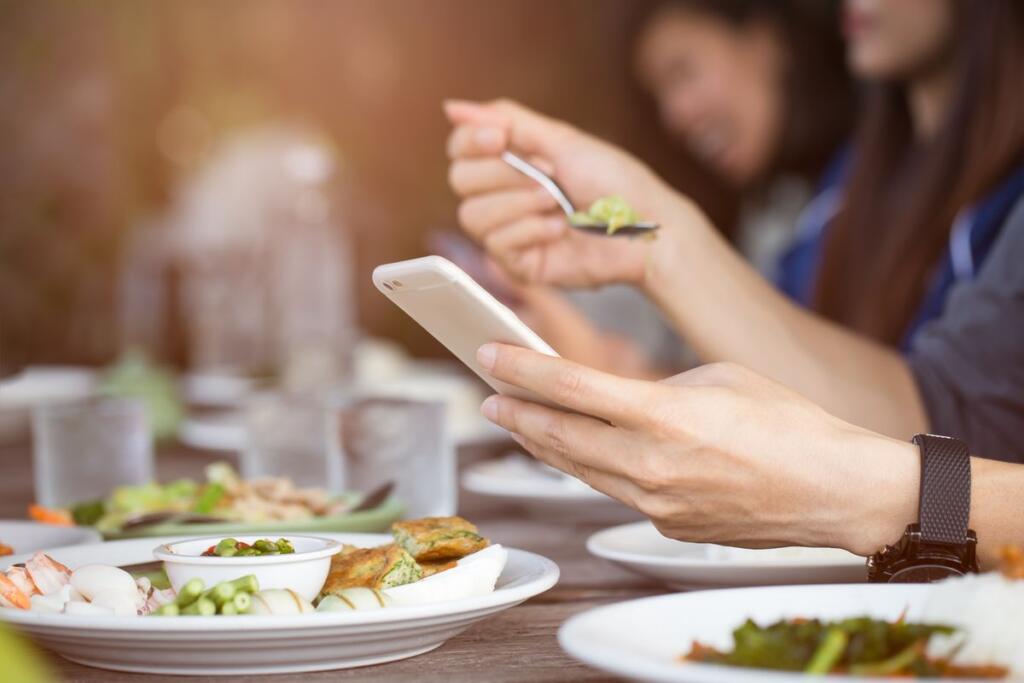 Una persona mangia al ristorante guardando i messaggi sullo smartphone