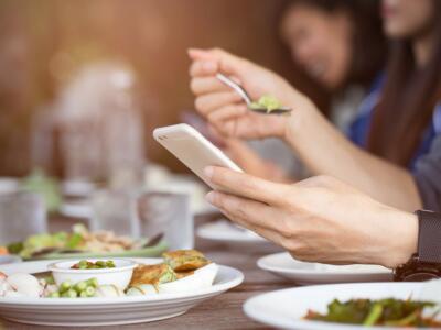 Una persona mangia al ristorante guardando i messaggi sullo smartphone
