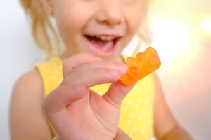 Una bambina con in mano la caramella di un orsetto gommoso
