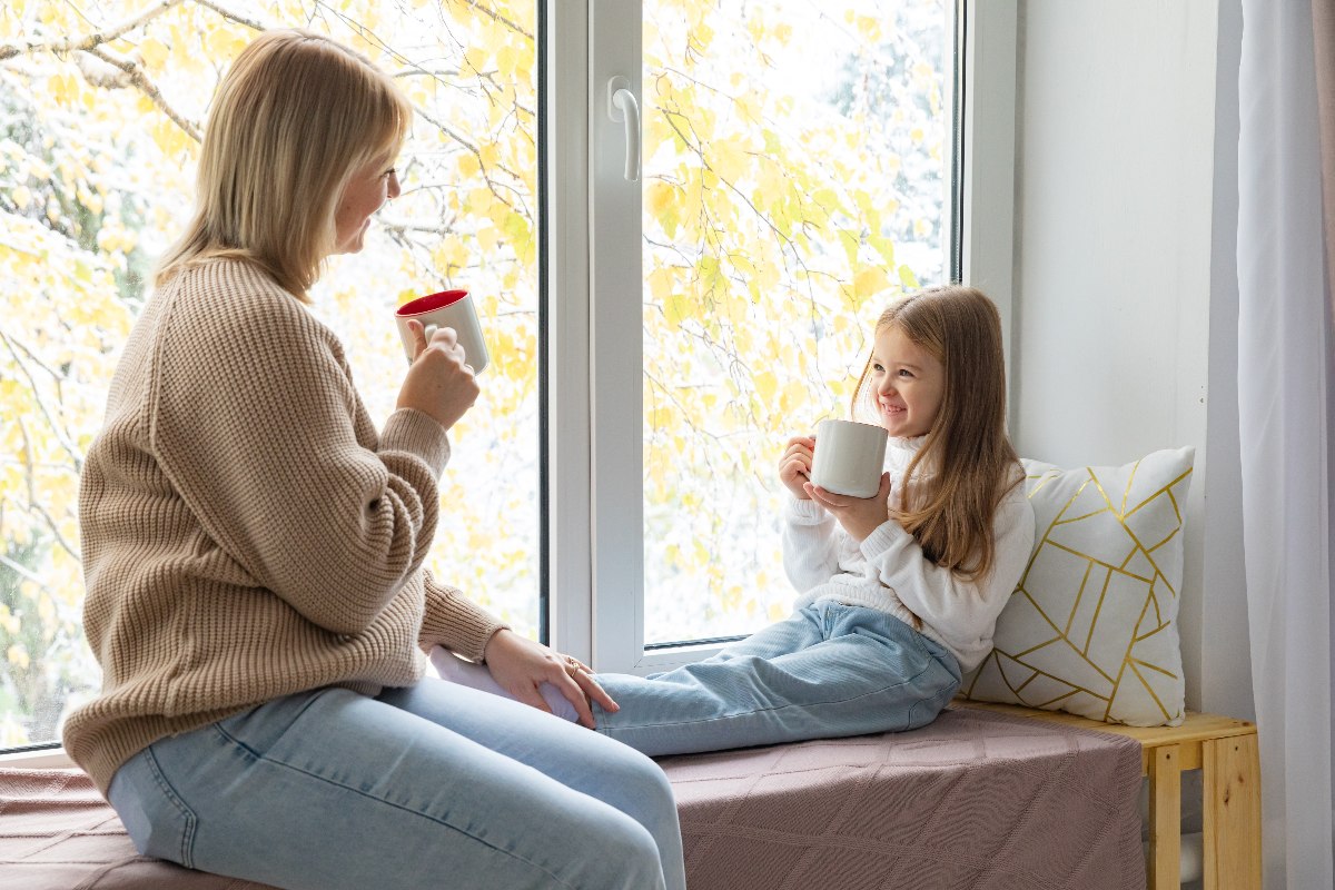 Mamma e figlia alla finestra con tazze