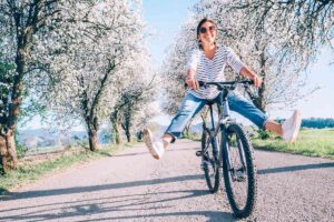 Donna felice in bicicletta tra alberi in fiore primaverili