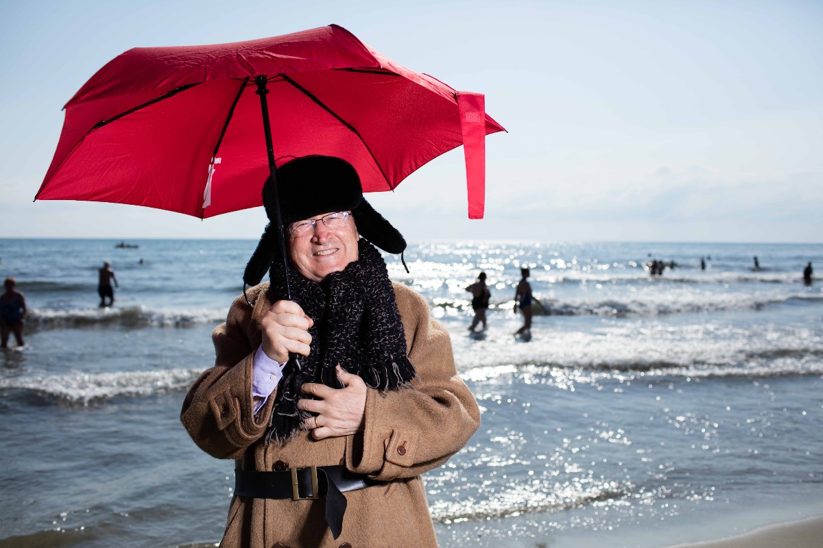 Con 36°C, il meteorologo Mario Giuliacci si presenta in spiaggia al Bagno Firenze con cappotto, cappello e ombrello.