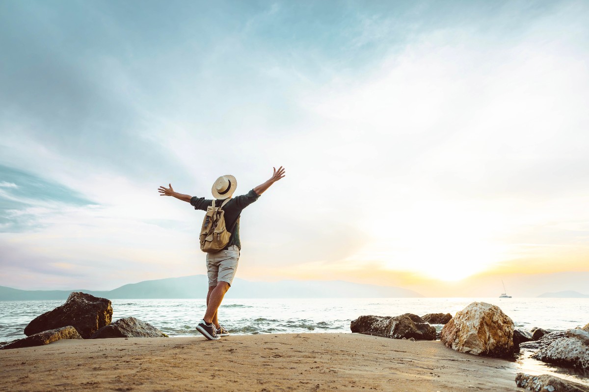 Ragazzo in piedi sulla spiaggia dopo una passeggiata, osserva il mare al tramonto.