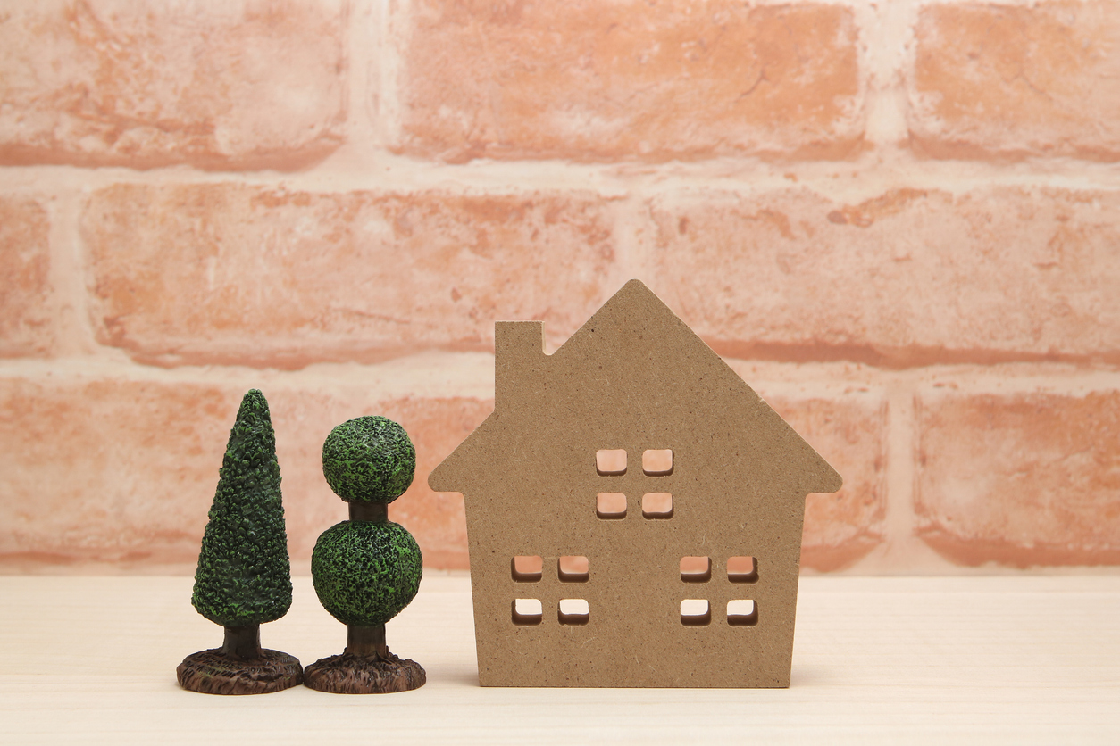 Miniature house and trees in front of brick wall.